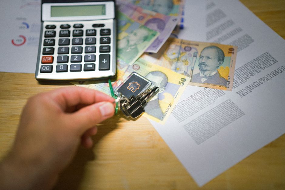 A clean, modern flat lay of a calculator, house keys, and a pen on a wooden table, symbolizing the financial decision-making involved in selling a home.